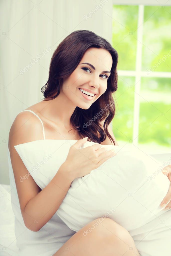 Young beautiful smiling woman waking up with pillow, at bedroom