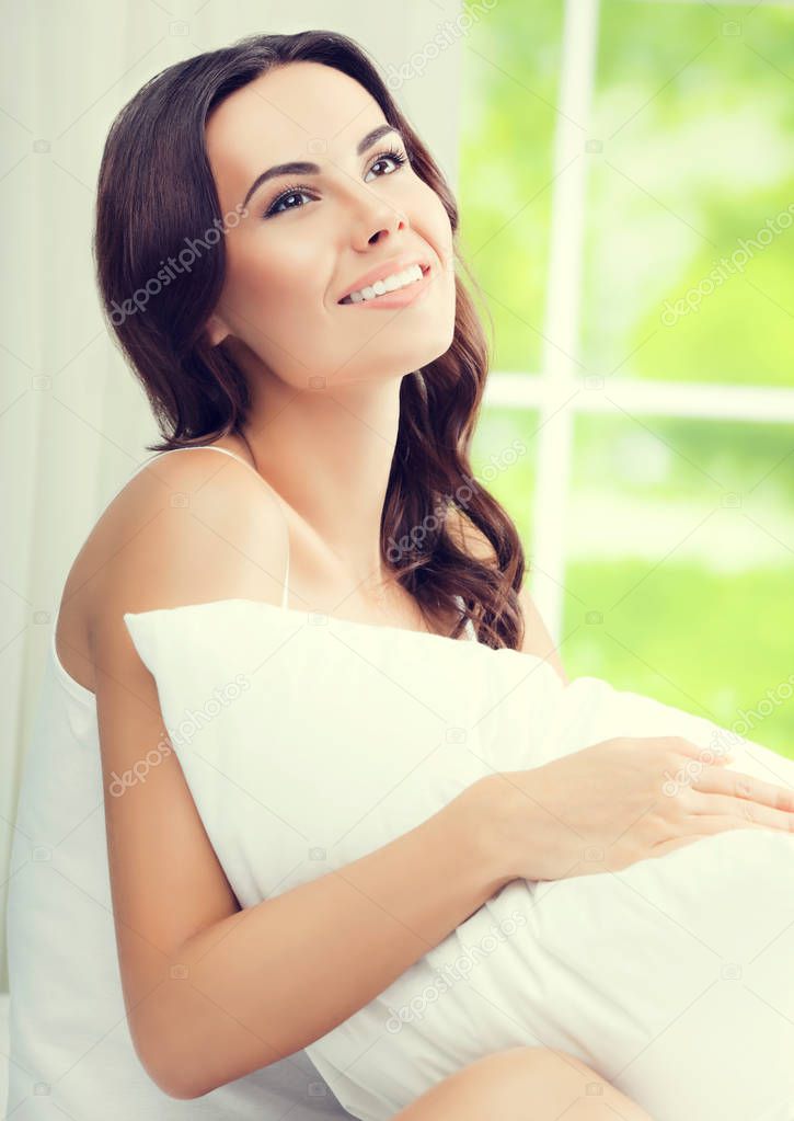 Young beautiful smiling woman waking up with pillow, at bedroom