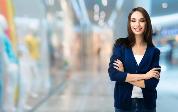 Giovane donna sorridente con le braccia incrociate, al centro commerciale — Foto Stock