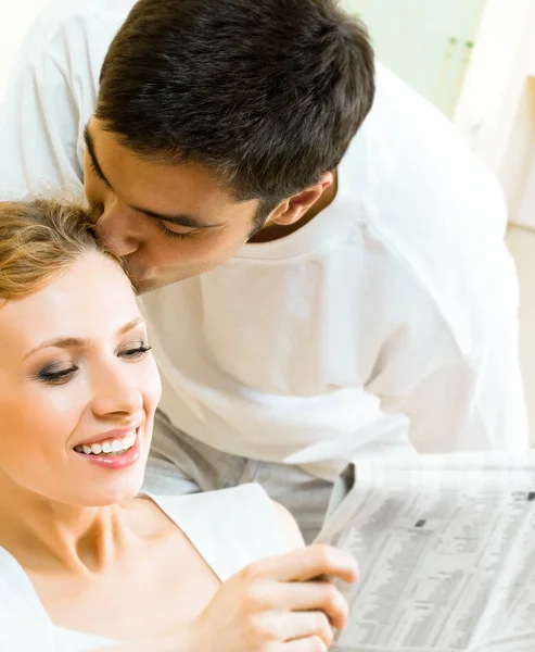 Young happy amorous couple reading newspaper at home — Stock Photo, Image