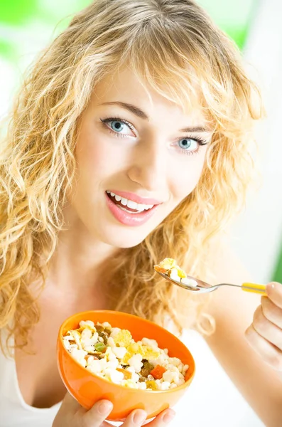 Porträt einer jungen lächelnden Frau, die Müsli oder Cornflakes isst, drinnen — Stockfoto