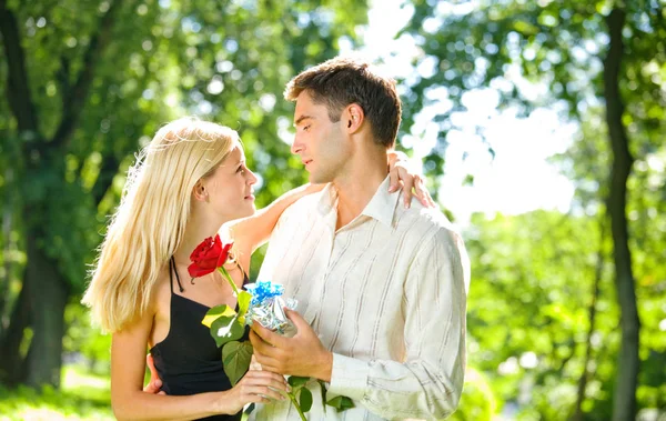 Casal feliz com presente e rosa, ao ar livre — Fotografia de Stock