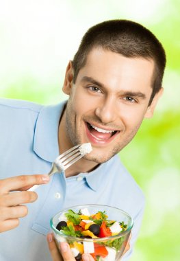 Genç mutlu adam yeme salata, açık havada