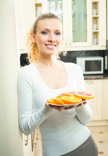 Vrouw met plaat van sinaasappels en grapefruit thuis — Stockfoto