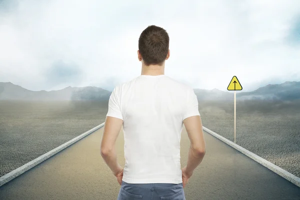 Casual young man standing on road with forward sign on abstract landscape background. Success concept — Stock Photo, Image
