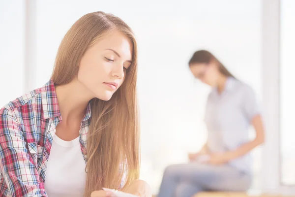 Portrait de jeune fille attentive en chemise décontractée sur fond lumineux avec une autre femme — Photo