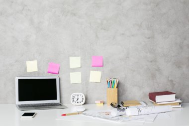 Boş dizüstü bilgisayar, akıllı telefon, iş skeçler, sarf malzemeleri ve beton duvar arka plan üzerinde diğer öğeleri ile Tasarımcı işyeri. Alay etmek