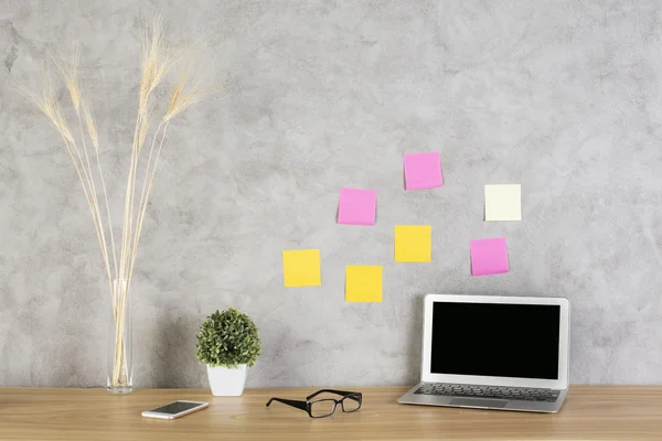 Front view of laptop on wooden desktop with glasses, smartphone and decorative plants on concrete wall background with colorful stickers. Mock up — Stock Photo, Image