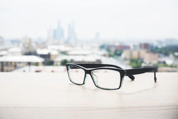 关闭的眼镜放在木制表面。模糊的城市视图背景 — 图库照片