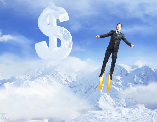 Young superman flying in bright blue sky with creative dollar sign above snowy mountains. Success concept — Stock Photo, Image