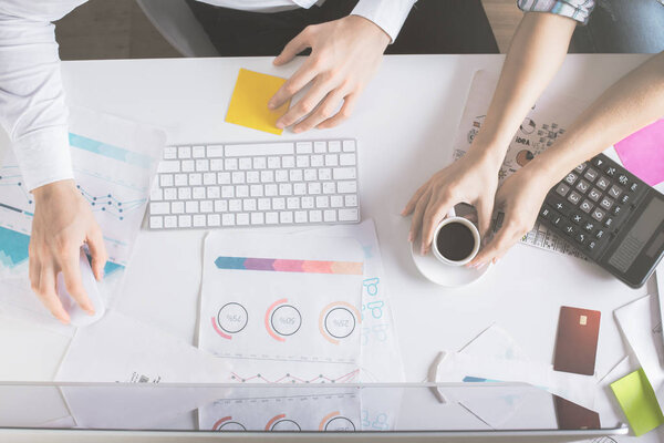 Вид сверху на белый рабочий стол с мужчиной и женщиной, держащими чашку кофе, использующими компьютер и работающими с бумагой. Концепция командной работы
