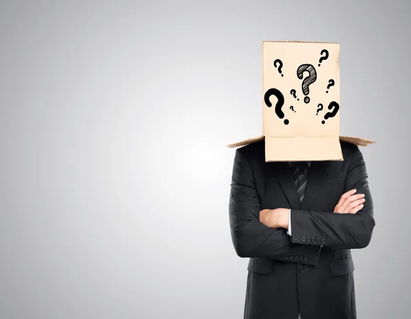 Businessman with folded arms and cardboard box with question marks covering head on grey background. Confusion concept — Stock Photo, Image