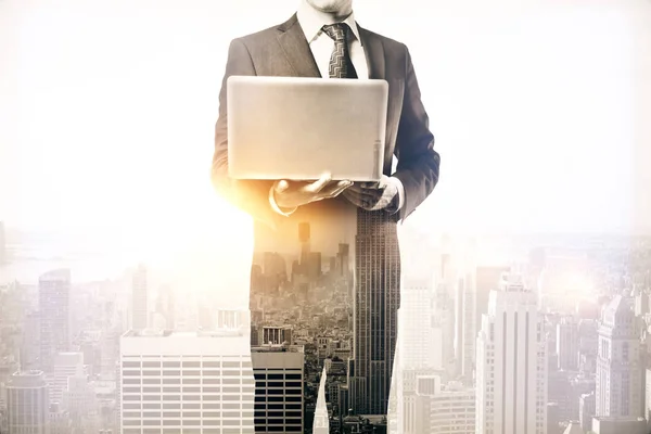 Uomo d'affari che tiene il computer portatile su sfondo astratto della città con la luce del sole. Il concetto di comunicazione. Doppia esposizione — Foto Stock