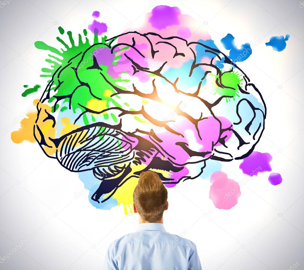 Young man looking at creative colorful brain sketch on light background. Brainstorming concept
