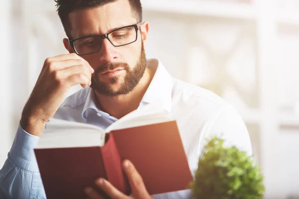 Portrait rapproché d'un homme européen attrayant lisant un livre sur un lieu de travail moderne avec des plantes décoratives et d'autres objets. Concept d'éducation — Photo