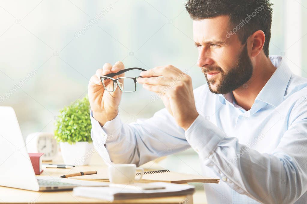 Attractive caucasian businessman looking at laptop screen throught spectacle lenses. Research concept