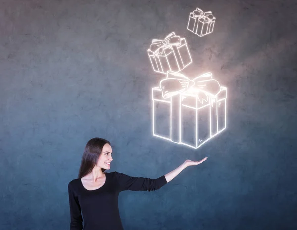 Retrato lateral de una atractiva mujer sonriente sosteniendo cajas de regalo abstractas dibujadas e iluminadas sobre fondo de hormigón. Concepto sorpresa —  Fotos de Stock