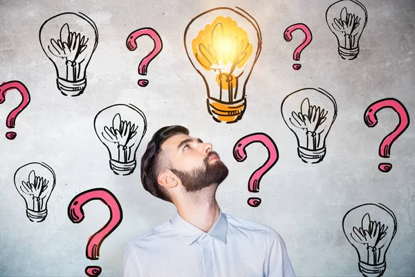 Portrait of curious young man on concrete background with drawn lamps and red question marks. Idea concept — Stock Photo, Image