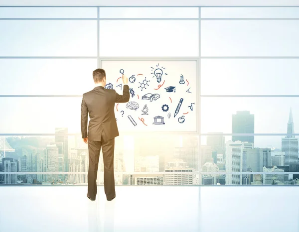 Back view of businessman drawing education related icons on whiteboard in modern office with city view and sunlight. Science concept. 3D Rendering — Stock Photo, Image