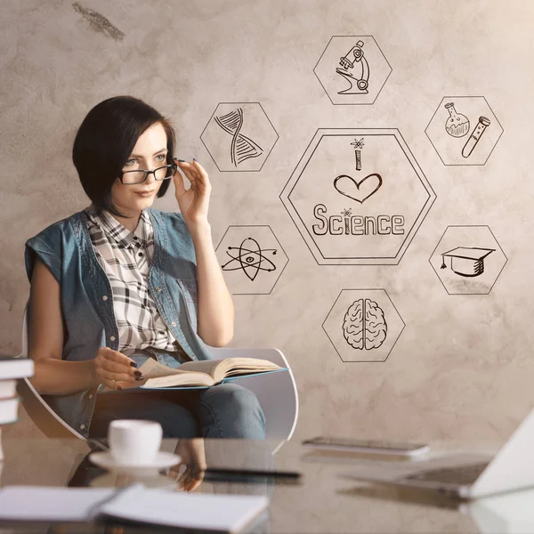 Atractivo libro de lectura mujer caucásica en el lugar de trabajo con boceto creativo, portátil, taza de café y otros artículos. Concepto científico —  Fotos de Stock