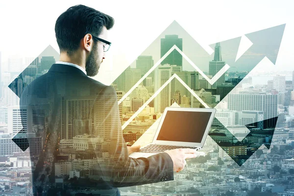 Vista posterior de un joven hombre de negocios que usa una computadora portátil en blanco sobre fondo abstracto de la ciudad con flechas. Concepto de crecimiento. Prepárate. Doble exposición —  Fotos de Stock