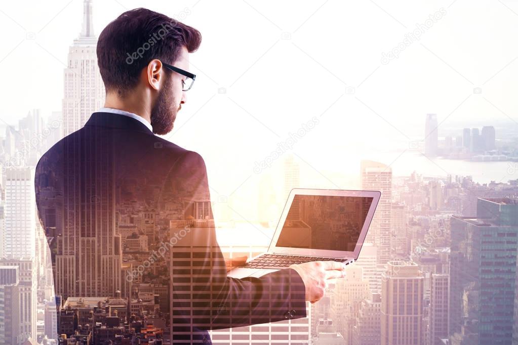 Back view of young businessman using blank laptop on abstract city background. Career concept. Mock up. Double exposure