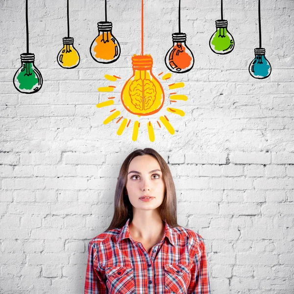 Portrait of attractive thoughtful european girl on brick background with drawn light bulbs. — Stock Photo, Image