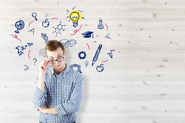 Portret van nadenkende jongeman op houten achtergrond met onderwijs pictogrammen. — Stockfoto