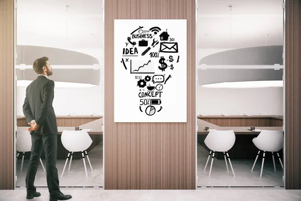 Jovem empresário em interior de madeira moderna olhando para quadro branco com esboço de negócios. Conceito de ideia . — Fotografia de Stock