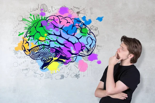 Vista lateral de un joven reflexivo mirando un dibujo creativo del cerebro sobre un fondo concreto . —  Fotos de Stock