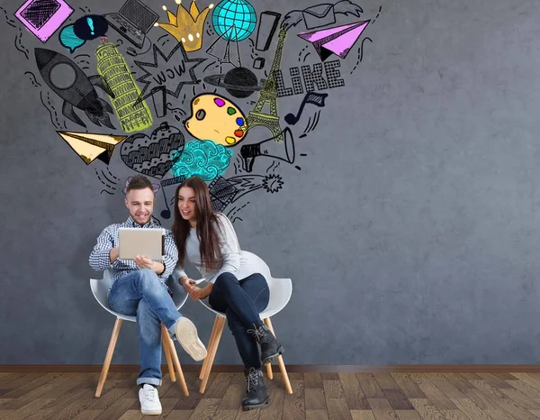 Joli jeune homme et jeune femme assis sur des chaises et utilisant un ordinateur portable ensemble dans la chambre avec un croquis des médias sociaux. Concept de communication — Photo