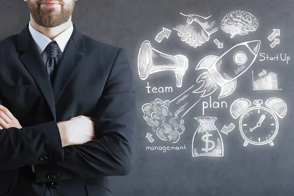 Portrait of thoughtful european businessman with folded arms standing on concrete background with business sketch. Success concept — Stock Photo, Image