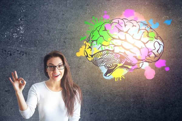 Gelukkig Europees meisje ok gebaar waarop conccrete achtergrond met kleurrijke hersenen schets. Brainstormen concept — Stockfoto