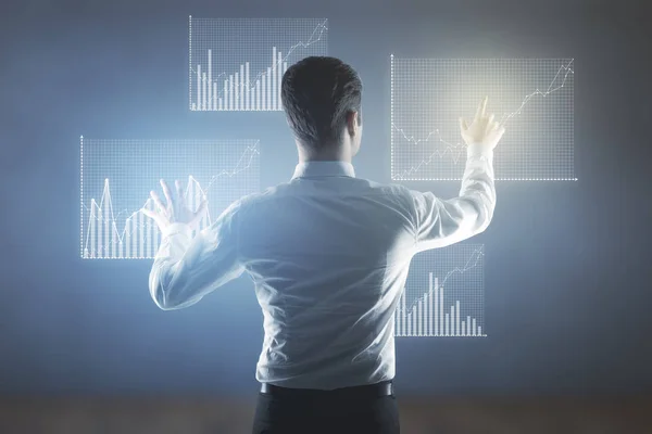 Back view of young businessman on blurry background managing business charts. Economy concept — Stock Photo, Image