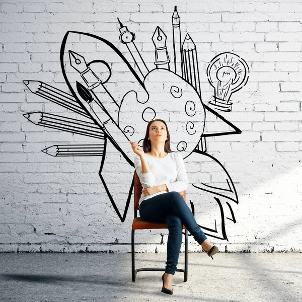 Thoughtful woman sitting on chair in white bricj room with creative sketch on wall. Art concept