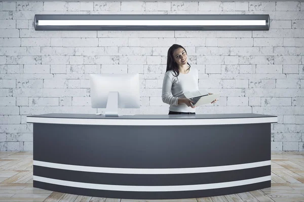 Atraktivní mladá žena v recepci s zařízení pomocí přenosného počítače. Cihlová zeď na pozadí. Koncepce ministra. 3D vykreslování — Stock fotografie