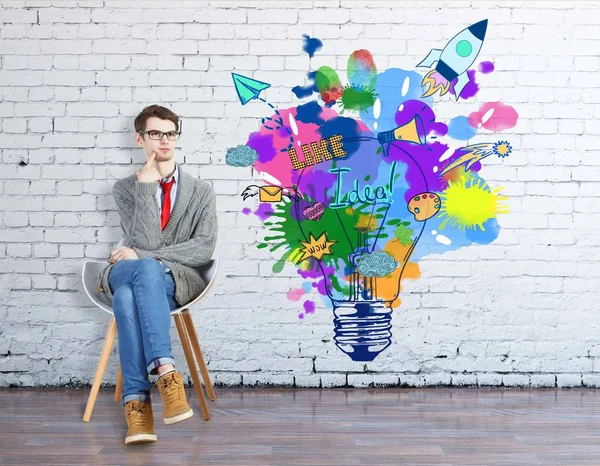 Ragazzo premuroso seduto sulla sedia all'interno con luminoso schizzo di lampada sul muro di mattoni. Concetto di avvio — Foto Stock