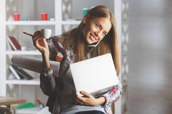 Retrato de una chica bastante caucásica usando un portátil, tomando café y hablando por teléfono en el lugar de trabajo. Concepto de comunicación — Foto de Stock