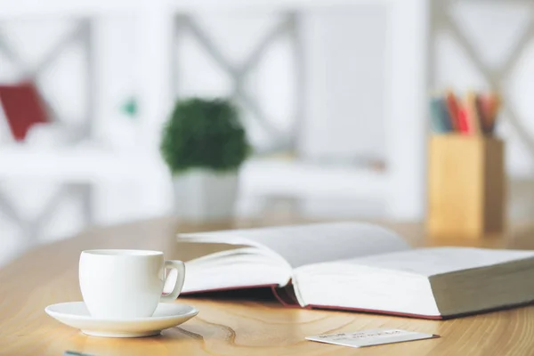 Primer plano de escritorio de oficina de madera con taza de café de cerámica, libro abierto, planta borrosa, suministros y otros artículos. Concepto de conocimiento —  Fotos de Stock