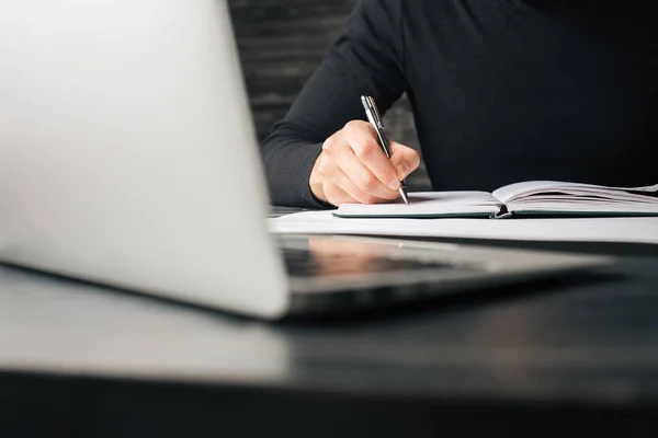 Mannenhand schrijven in Kladblok op donkere houten tafel met opengeklapte laptop geplaatst. Papierwerk concept — Stockfoto