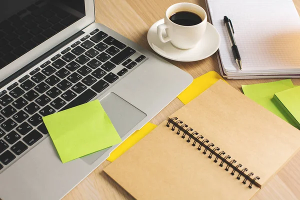 Primo piano del posto di lavoro ufficio con laptop, tazza di caffè, blocco note a spirale e adesivi colorati — Foto Stock