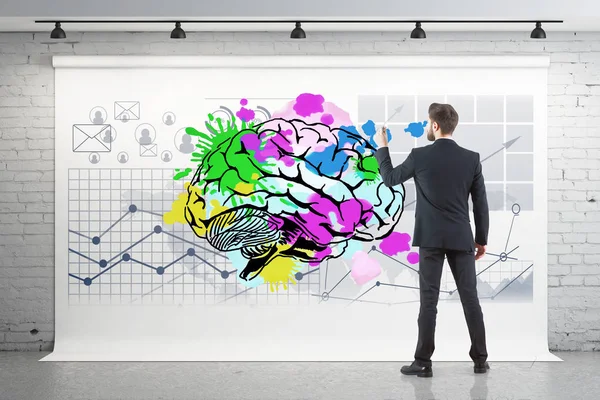 Вид ззаду молодого бізнесмена, який малює барвистий мозок і бізнес-чарти на плакаті, що звисає в цегляному інтер'єрі. Концепція мозкового штурму. 3D рендерингу — стокове фото