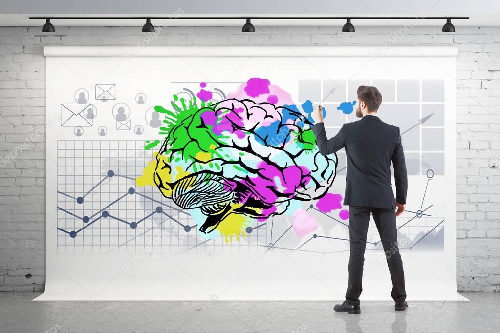 Back view of young businessman drawing colorful brain and business charts on poster hanging in brick interior. Brainstorming concept. 3D Rendering