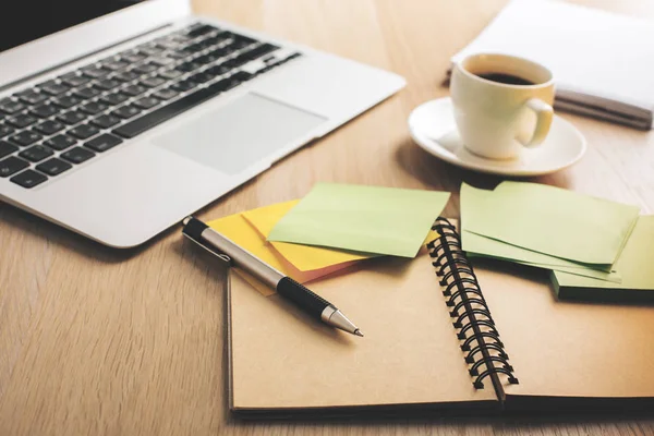 Primo piano del tavolo da ufficio in legno con computer portatile, tazza di caffè, blocco note a spirale e adesivi colorati — Foto Stock