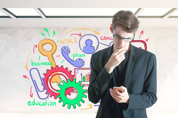 Bonito jovem empresário usando smartphone no interior com esboço colorido na parede. Conceito de comunicação. Renderização 3D — Fotografia de Stock