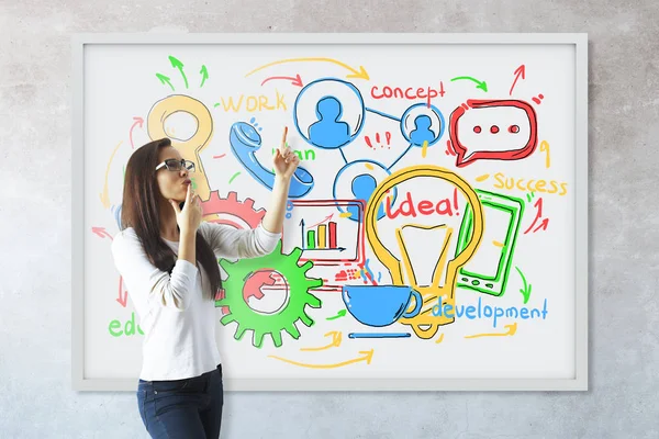 Mujer joven reflexiva apuntando a pizarra blanca con boceto de negocios. Fondo de pared de hormigón. Concepto de comunicación . — Foto de Stock