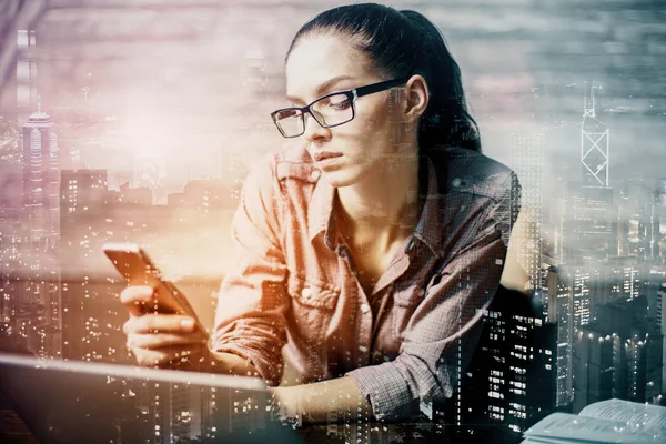 Mujer joven usando smartphone en el lugar de trabajo. Concepto de comunicación. Fondo de la ciudad. Doble exposición — Foto de Stock