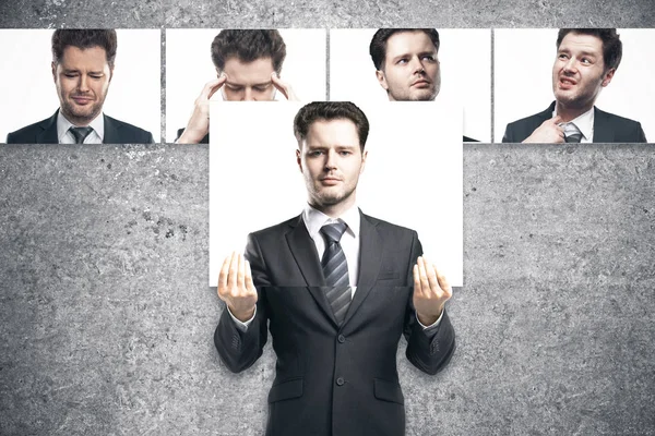 Jeune homme d'affaires européen se cachant traîneau derrière une affiche au visage droit. Rangée de visages avec différentes expressions en arrière-plan. Concept d'émotion — Photo