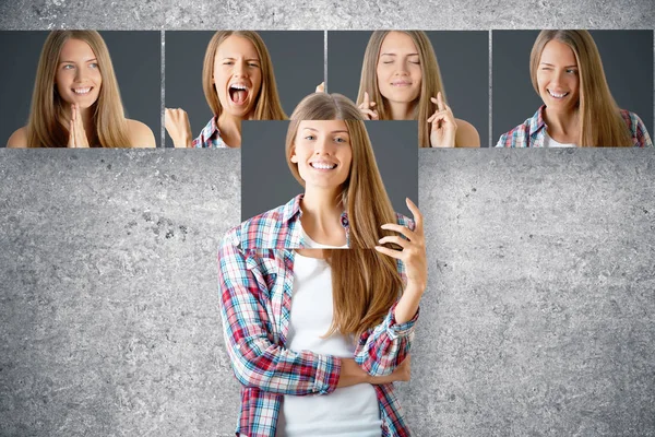 Junge europäische Geschäftsfrau versteckt sich hinter einem Plakat mit lächelndem Gesicht. Reihe von Gesichtern mit unterschiedlichen Ausdrücken im Hintergrund. Emotionales Konzept — Stockfoto