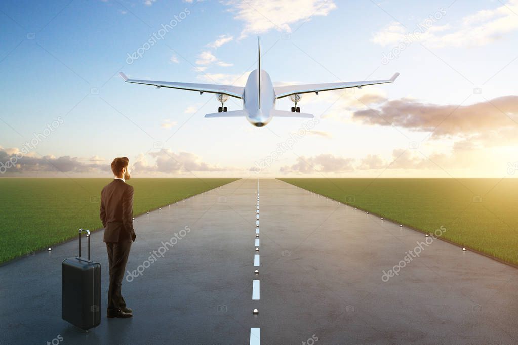 Businessman with luggage standing on runway with taking off airplane. Sky backgroiund. Travel concept. 